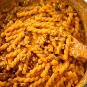 sausage and bacon pasta in large pot with wooden spoon digging in
